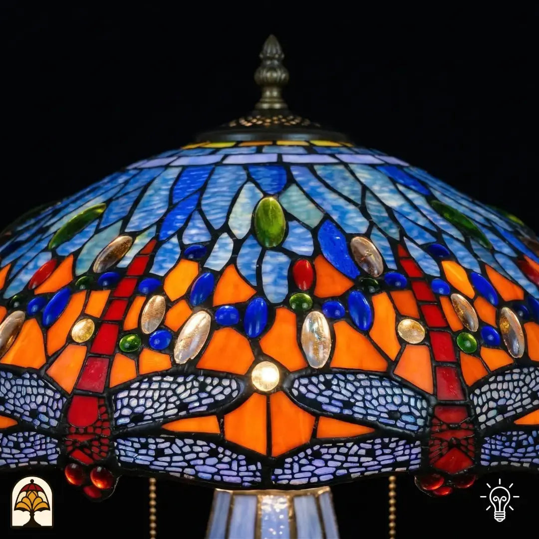 Gros plan de lampe Tiffany, zone supérieure de l'abat-jour allumée, verre bleu et bleu clair avec cabochons en verre ovales bleus, verts et ambrés en bande, fleuron pointu visible en haut