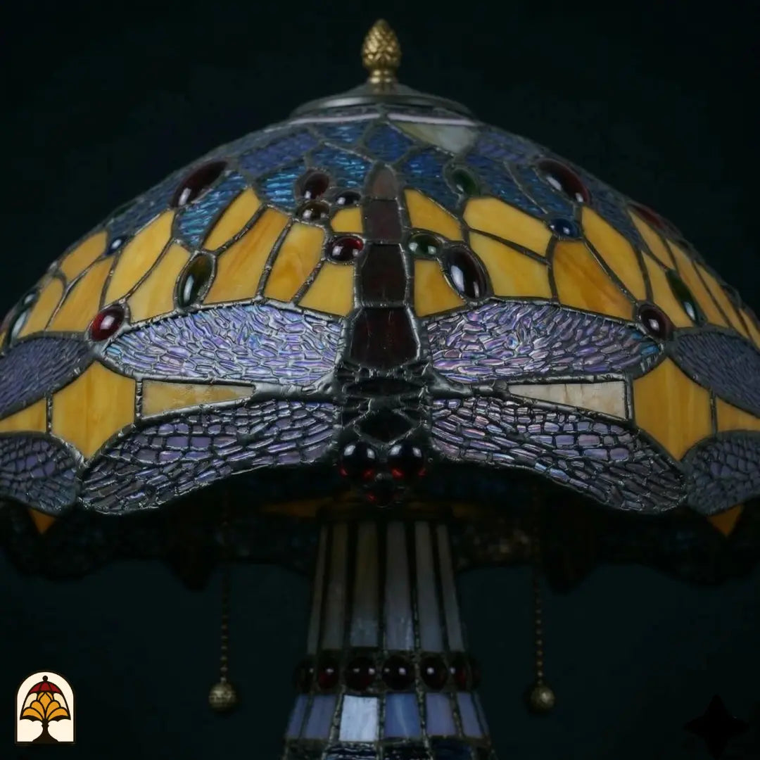 Gros plan abat-jour lampe de table Tiffany Libellula Azurea ⌀30 cm – motif de libellules aux ailes bleues, vitrail ambré et cabochons en verre rouges, bouton en bronze en forme de pomme de pin
