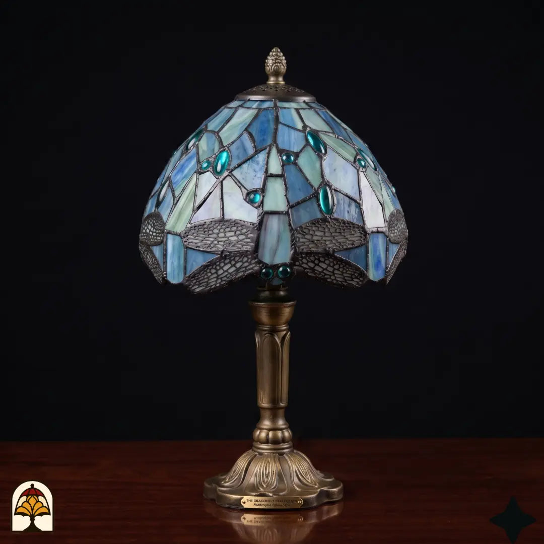 Lampe de table Tiffany Libellula Celeste ⌀20 cm éteinte sur une table en bois – abat-jour en vitrail bleu à motif de libellule et cabochons en verre turquoise, pied colonne en bronze