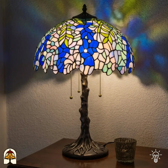 Verlichte Tiffany tafellamp Wisteria Celeste ⌀40 cm in interieur – blauwe en witte glyciniabloemen in glas-in-lood, bronzen boomstam voet, warm licht