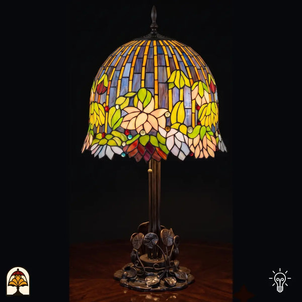 Lampe de table Tiffany Pond Lilia ⌀40 cm allumée sur fond noir – nénuphars dans un abat-jour en vitrail crème et vert, pied en bronze à motif de feuille de nénuphar