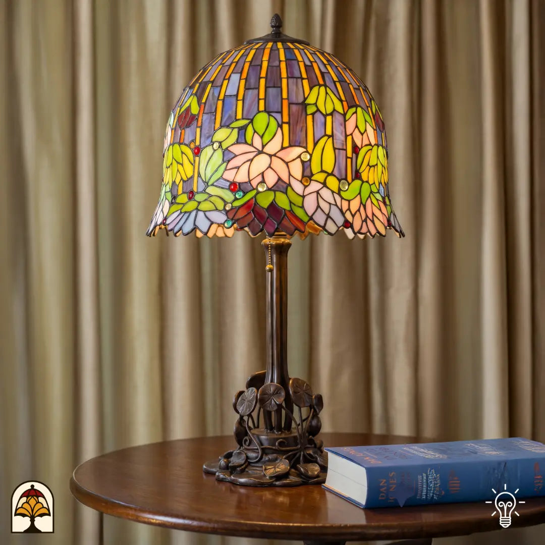 Lampe de table Tiffany Pond Lilia dans un intérieur chaleureux sur une table d'appoint ronde – abat-jour en vitrail à nénuphars allumé, pied en bronze à motif de feuilles