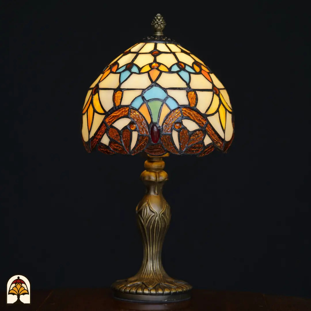 Lampe de table Tiffany Baroque ⌀20 cm allumée sur fond noir – abat-jour en dôme crème avec feuillages baroques ambrés, formes arquées bleu clair et pierre précieuse rouge, pied Art nouveau en bronze ouvragé