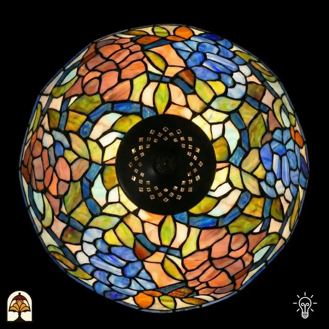 Vue de dessus abat-jour dôme allumé lampe de table Tiffany Florentia Blu, motifs de feuilles orange-rose, bleus, verts et beiges en vitrail, douille centrale noire visible