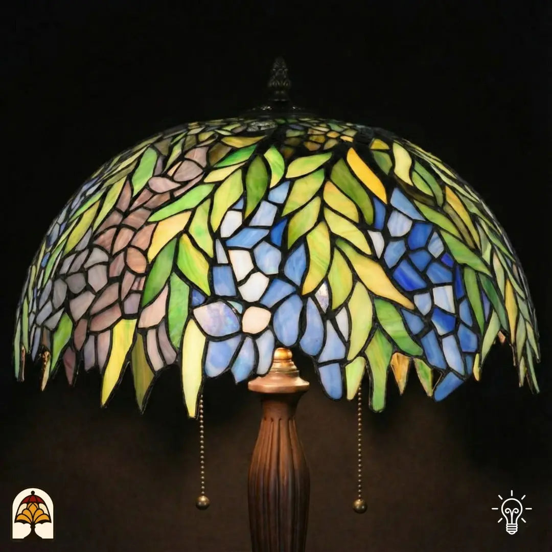 Gros plan abat-jour Tiffany allumé — feuilles vertes, fleurs bleues et roses/lilas (style glycine), accents jaunes