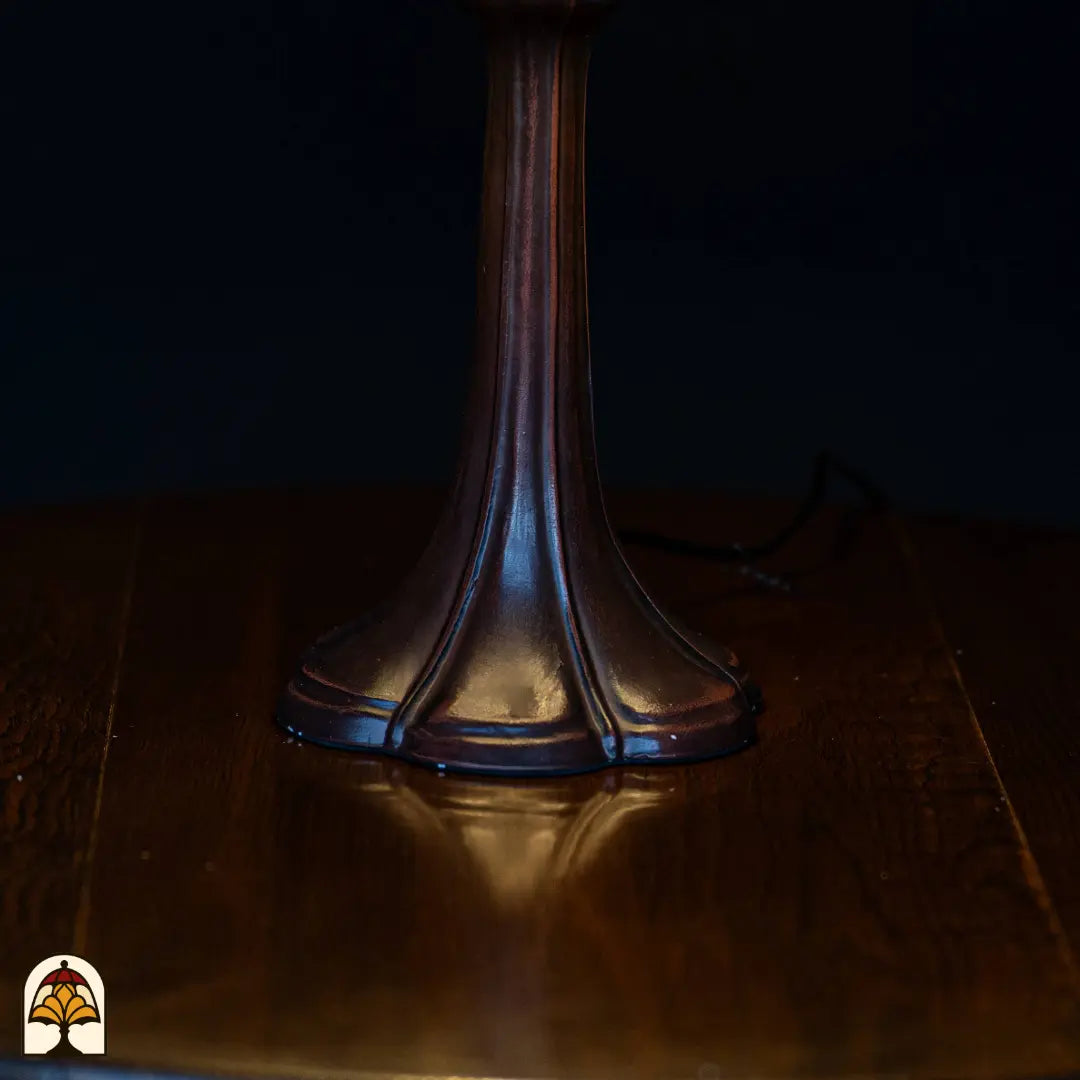 Gros plan pied trompette en bronze lampe de table Libellula Aurea ⌀30 sur plateau en bois, fond sombre, câble d'alimentation visible