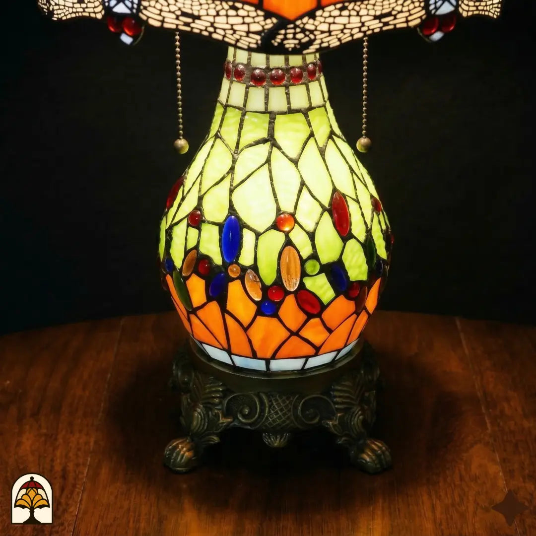 Gros plan du pied sphérique en vitrail allumé Libellula Lumina ⌀30, panneaux jaune-vert et orange avec cabochons ovales bleus et colorés, anneau bleu avec cabochons rouges, socle en bronze ouvragé à pattes de lion
