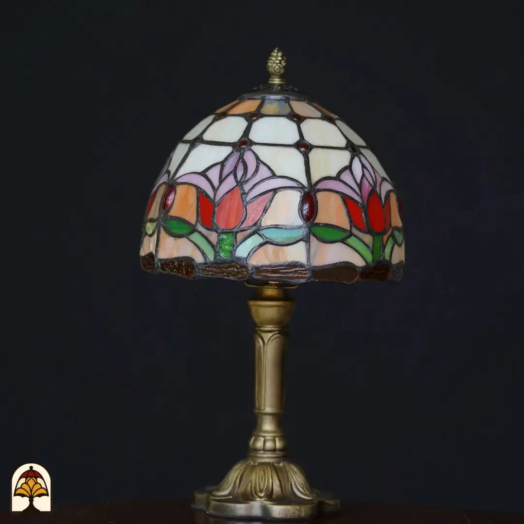 Lampe de table Tiffany Tulipa éteinte sur fond noir – abat-jour dôme avec tulipes roses, lilas et rouges sur verre crème, pied colonne en bronze à relief floral