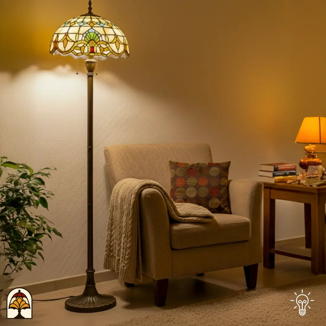 Lampadaire Tiffany Barok allumé dans un salon — à côté d'un fauteuil beige avec plaid et coussin, plante verte à gauche, table d'appoint avec livres à droite