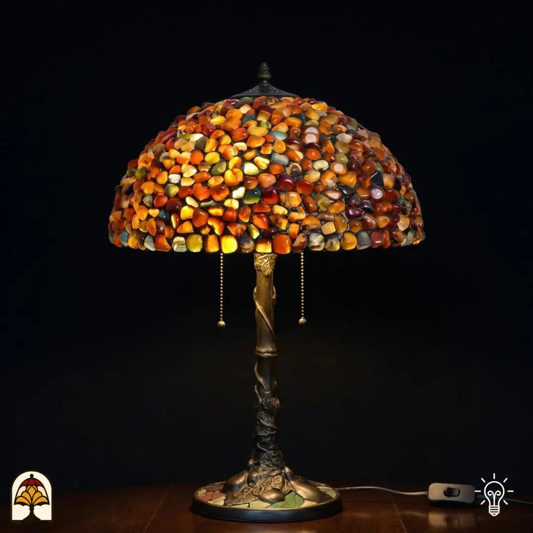 Lampe de table Tiffany Stone Mosaic Amber ⌀40 cm allumée sur fond sombre – abat-jour en dôme en pierres polies ambrées, orange et ocre, pied en forme de tronc d'arbre en bronze avec deux interrupteurs à chaînette