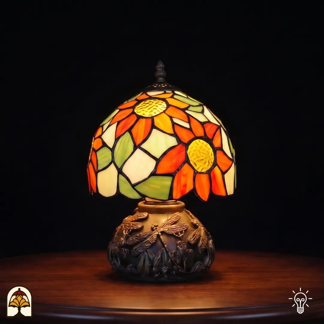 Lampe de table Tiffany Solea Radix ⌀20 cm allumée – abat-jour sphérique avec tournesols orange et feuilles vertes sur pied à libellules