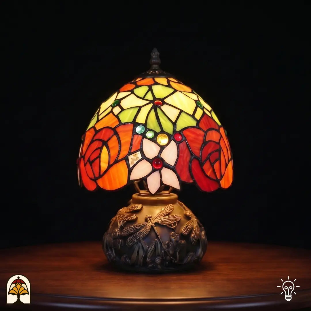 Lampe de table Tiffany Viola Ember ⌀20 cm allumée – abat-jour sphérique avec roses orange-rouge, feuilles vertes sur pied à libellules