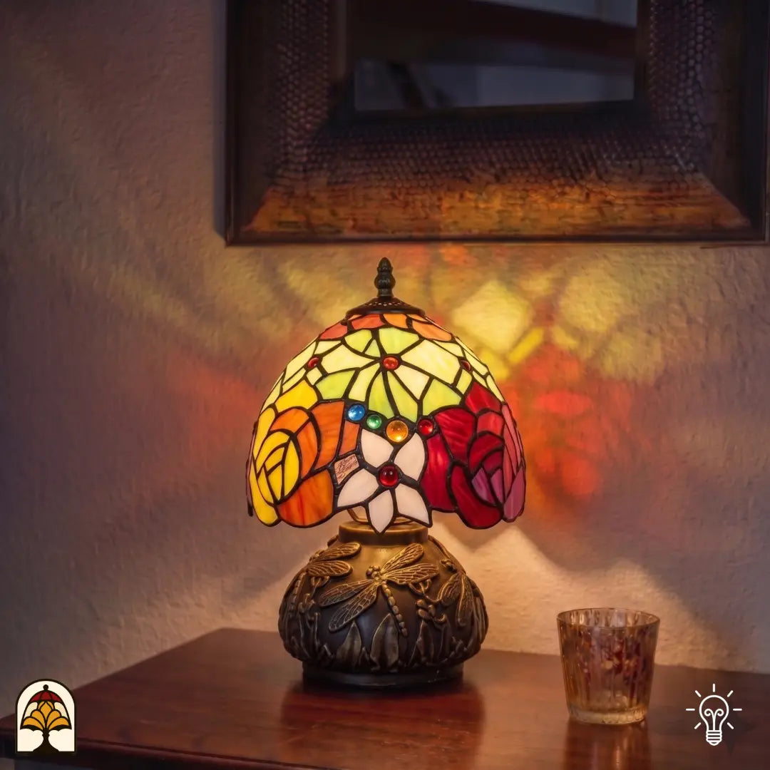 Lampe de table Tiffany Viola Ember allumée dans un intérieur chaleureux – jeu de couleurs vif de roses sur pied à libellules