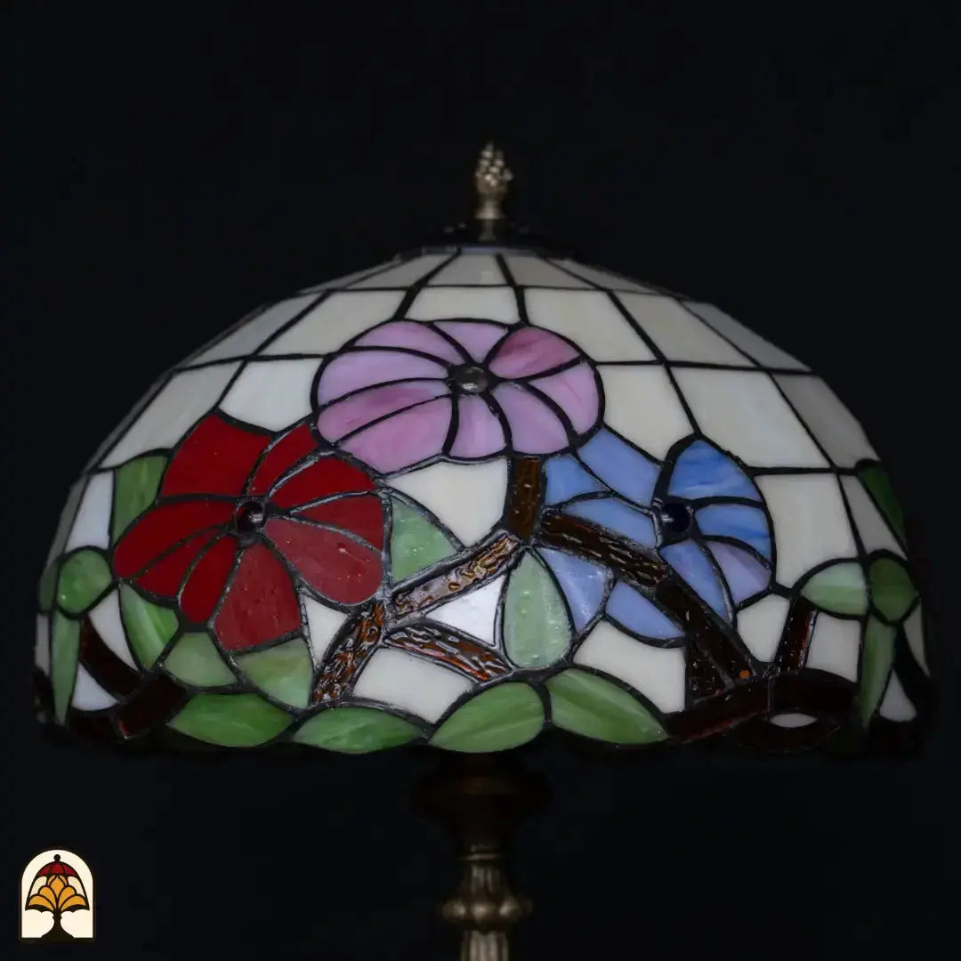 Gros plan abat-jour lampe de table Tiffany Aurora Bloom éteinte — fond blanc avec fleurs roses, rouges et bleues, branches dorées/brunes, feuilles vertes