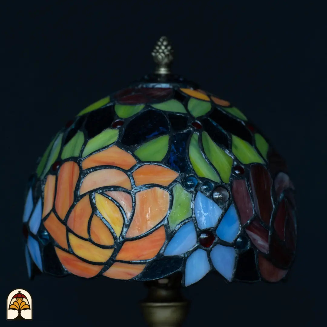 Gros plan abat-jour lampe de table Tiffany Fiore éteinte — roses orange et roses, feuilles vertes, fleurs bleues et bleu clair, pierres précieuses rouges