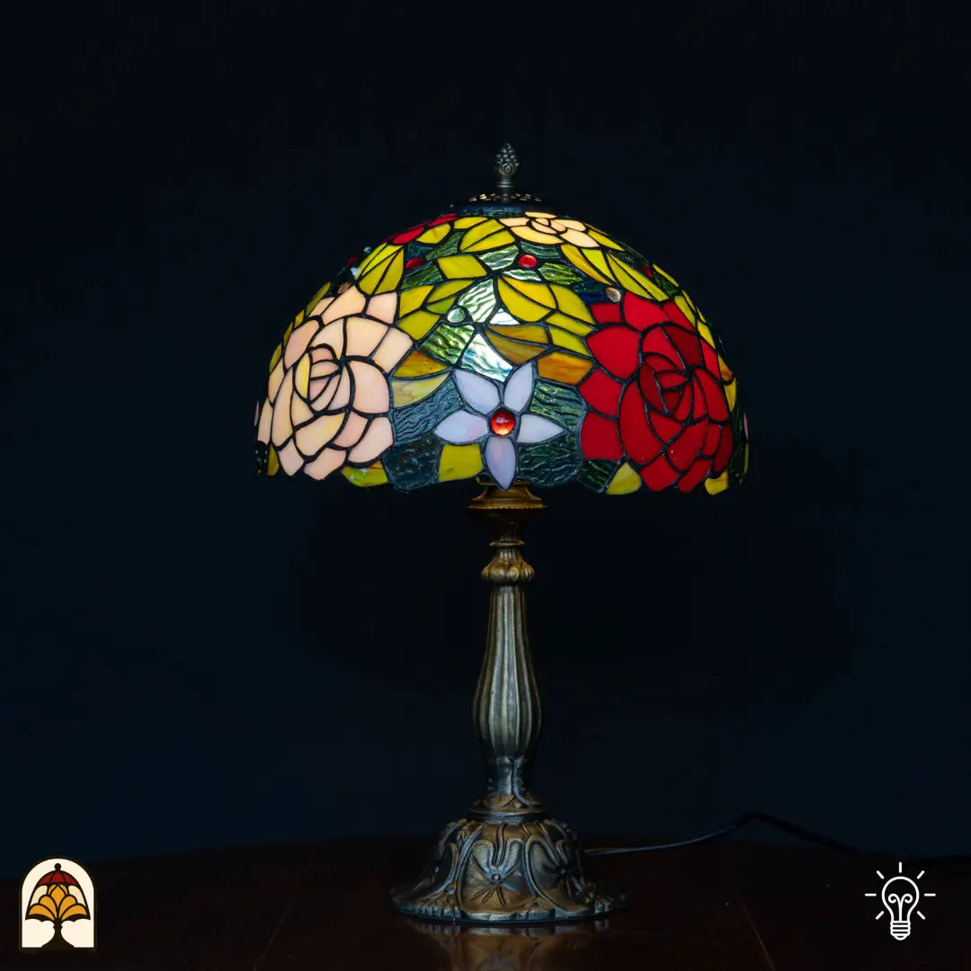 Lampe de table Tiffany Rosetta ⌀30 cm allumée sur fond noir – abat-jour en dôme à motif de rosace en vitrail, pied colonne en bronze