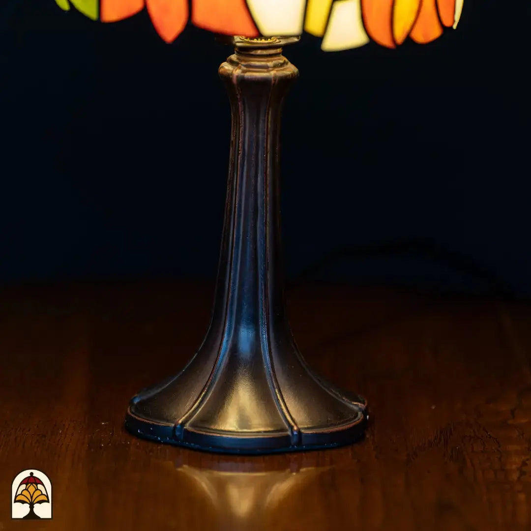 Gros plan pied lampe de table Tiffany Solea — pied en bronze Art Nouveau élancé et évasé avec fût cannelé, sur une table en bois