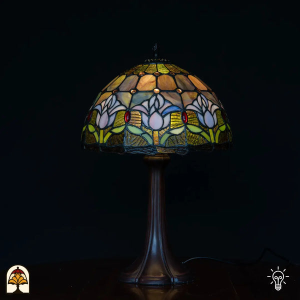 Lampe de table Tiffany Tulipa Lilac Sereno ⌀30 cm allumée sur fond noir – abat-jour en dôme avec tulipes lilas, pied colonne en bronze