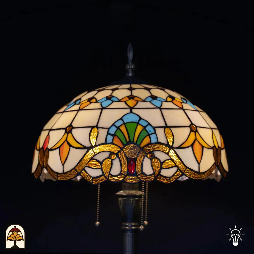 Gros plan abat-jour allumé lampadaire Tiffany Barok — verre crème/ambré, arche bleue centrale avec éventail vert, cabochon en verre rouge sur bordure en bronze, interrupteur à chaînette