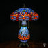 Tiffany lamp tafellamp verlicht, koepelvormige kap met blauw glas-in-lood bovenzone, oranje-rode middenzone met blauwe en amber glaskralen, lavendelblauwe libelle rand onderaan; peervormige lichtblauwe voet en bronzen leeuwenpootvoet