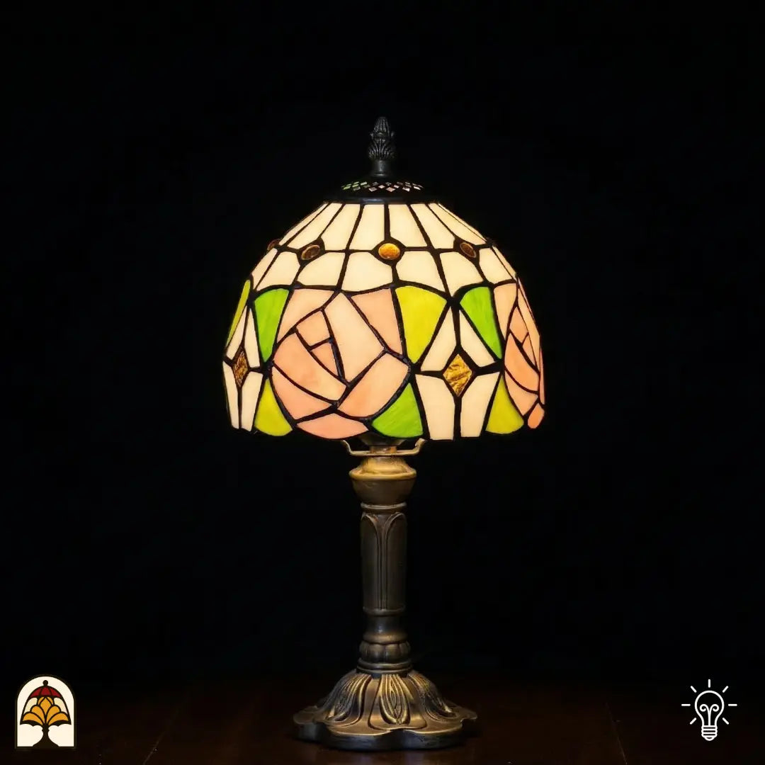 Petite lampe de table Tiffany Rosalia Verde allumée avec abat-jour en dôme, grande rose rose et feuilles vertes en vitrail, partie supérieure blanche avec accents ronds dorés, pied vase en bronze cannelé, fond sombre