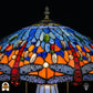 Detailopname van tiffany lamp kapbovenzone verlicht, blauw en lichtblauw glas met blauwe, groene en amber ovale glaskralen in een band, puntfinial bovenaan zichtbaar