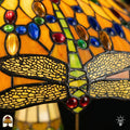 Detailopname van tiffany lamp libelle-rand onderaan de kap verlicht, geel-goudkleurige libellen met geaderde vleugels in glas-in-lood, blauwe en bruine ovale glaskralen en rode ronde kralen