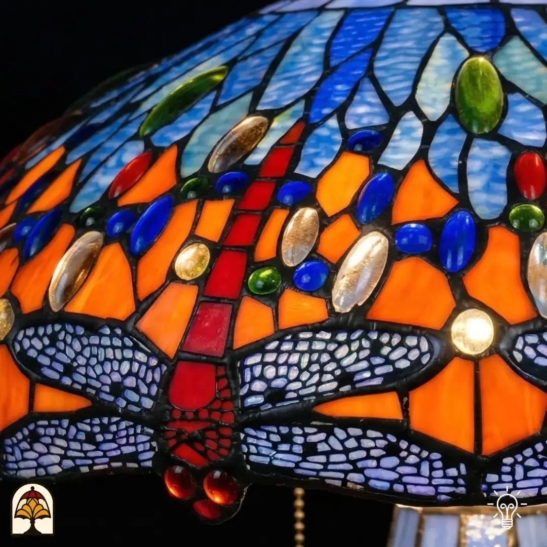 Gros plan de lampe Tiffany, bordure de libellules allumée en bas de l'abat-jour, libellules blanc-bleu lavande aux ailes nervurées en vitrail, libellules rouges visibles, cabochons en verre bleus et ambrés