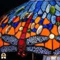 Detailopname van tiffany lamp libelle-rand onderaan de kap verlicht, lavendelblauw-witte libellen met geaderde vleugels in glas-in-lood, rode libellen zichtbaar, blauwe en amber glaskralen