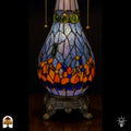 Detailopname van tiffany lamp glas-in-lood peervormige voet verlicht, lichtblauw glas met groene, blauwe en oranje glaskralen, trekketting zichtbaar en bronzen siervoet met leeuwenpoten
