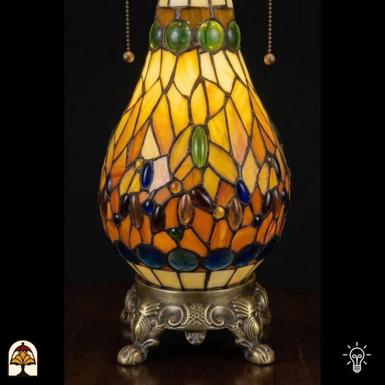 Detailopname van tiffany lamp glas-in-lood peervormige voet verlicht, amberkleurig glas met groene, blauwe en bruine ovale glaskralen, bronzen siervoet met leeuwenpoten en acanthusrolwerk