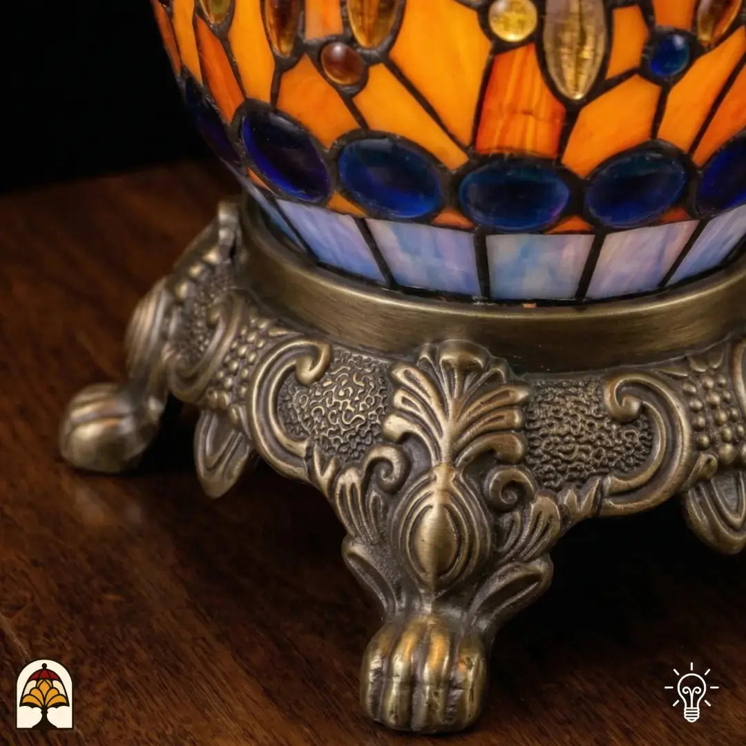 Gros plan de lampe Tiffany, pied décoratif en bronze à pattes de lion et ornement de feuilles d'acanthe, vitrail orange et bleu et cabochons en verre bleus visibles en haut