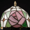 Close-up onverlichte kap Tiffany tafellamp Rosalia Verde, grote roze roos en groene bladeren in glas-in-lood