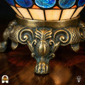 Detailopname van tiffany lamp bronzen siervoet met leeuwenpoten en acanthusblad-ornament, crème en oranje glas-in-lood en blauwe glaskralen bovenaan zichtbaar