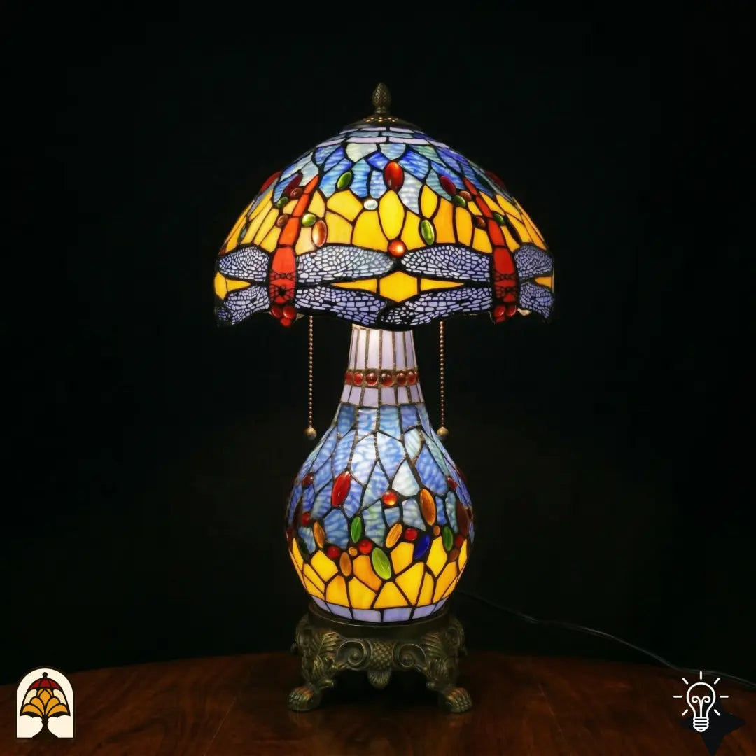 Lampe de table Tiffany Libellula Azurea ⌀30 cm allumée sur fond noir – abat-jour en dôme bleu azur à motif de libellule, pied colonne en bronze