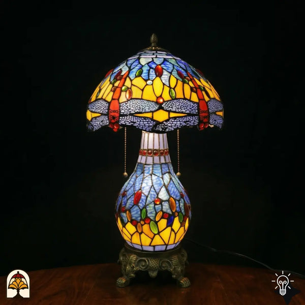 Lampe de table Tiffany Libellula Azurea ⌀30 cm allumée sur fond noir – abat-jour en dôme bleu azur à motif de libellule, pied colonne en bronze
