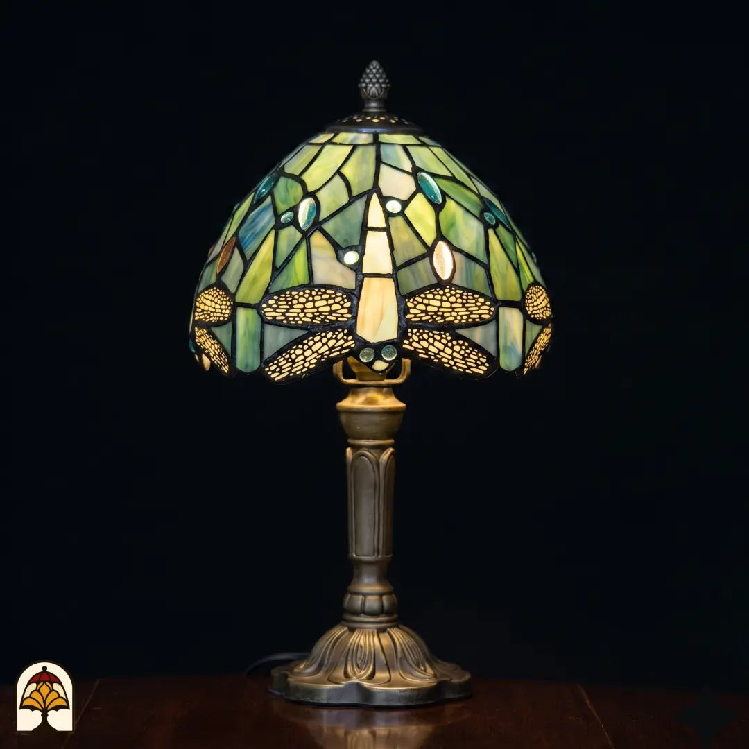 Lampe de table Tiffany Libellula Celeste ⌀20 cm allumée sur fond noir – abat-jour en dôme bleu clair à motif de libellule, pied colonne en bronze