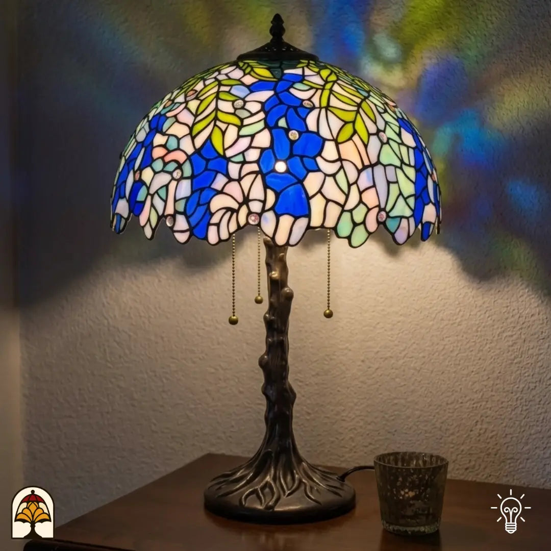 Lampe de table Tiffany Wisteria Celeste ⌀40 cm allumée dans un intérieur chaleureux – fleurs de glycine bleues et blanches en vitrail, pied en forme de tronc d'arbre en bronze, lumière chaude