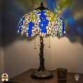 Verlichte Tiffany tafellamp Wisteria Celeste ⌀40 cm in interieur – blauwe en witte glyciniabloemen in glas-in-lood, bronzen boomstam voet, warm licht