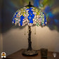 Verlichte Tiffany tafellamp Wisteria Celeste ⌀40 cm in interieur – blauwe en witte glyciniabloemen in glas-in-lood, bronzen boomstam voet, warm licht