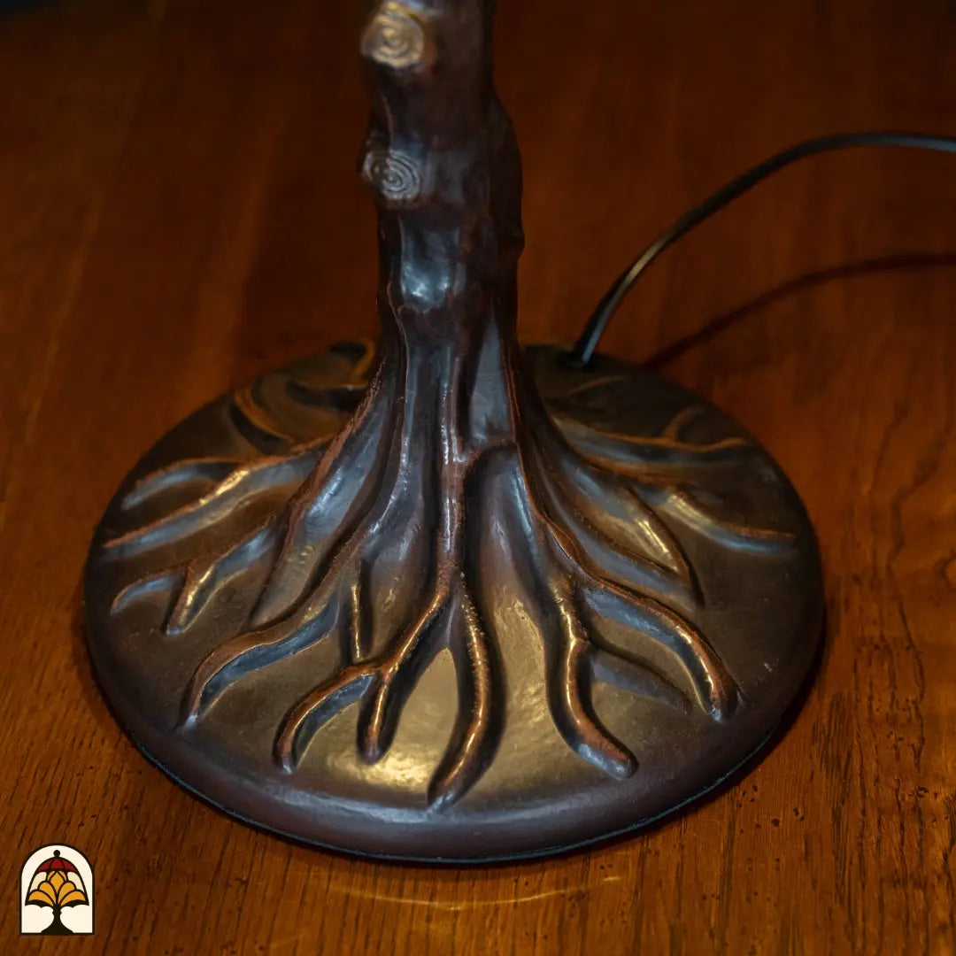 Gros plan pied en forme de tronc d'arbre en bronze Wisteria Celeste avec racines évasées sur base ronde, câble d'alimentation visible