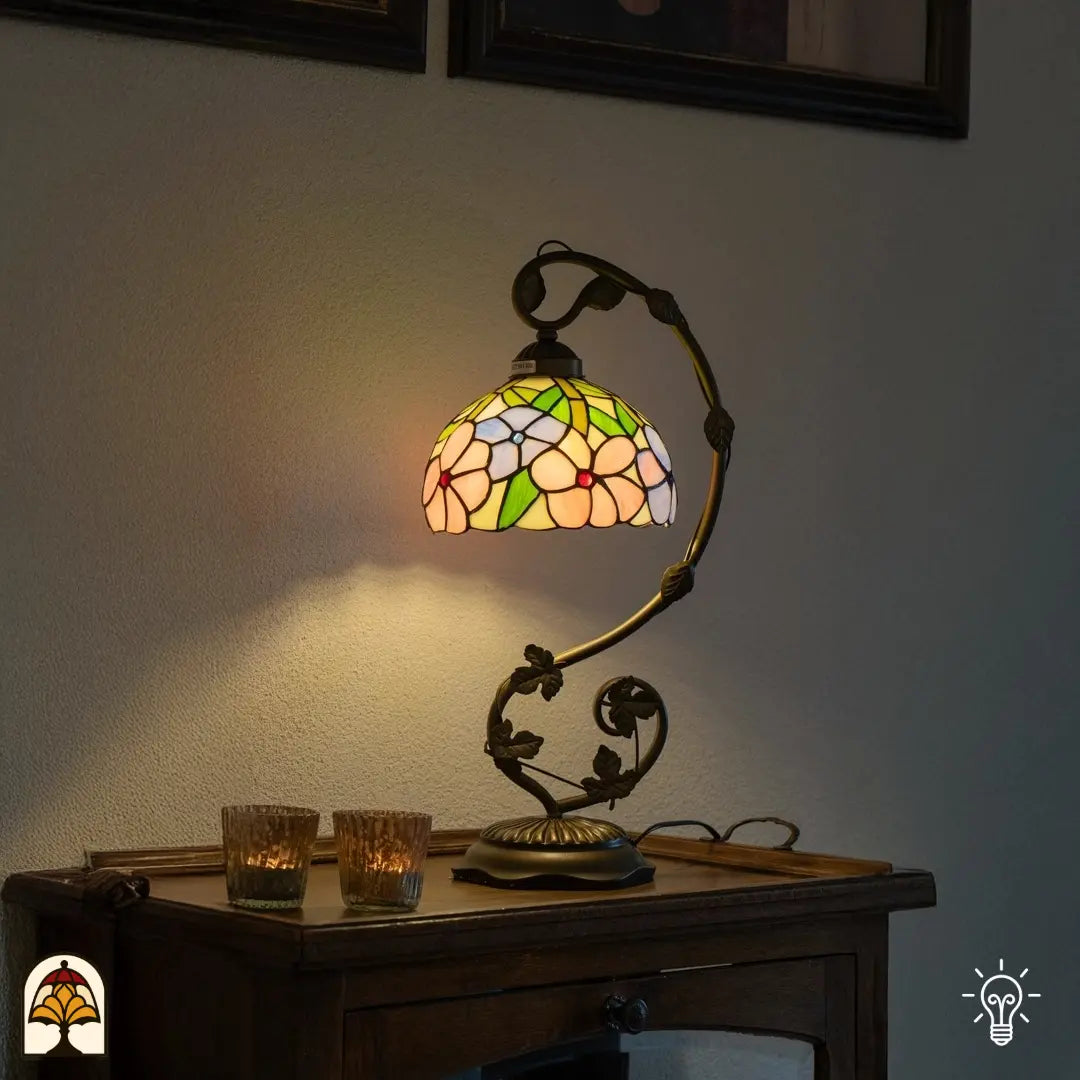Lifestyle — lampe de table Tiffany allumée sur une table d'appoint en bois devant un mur gris, deux bougies chauffe-plat en verre à côté