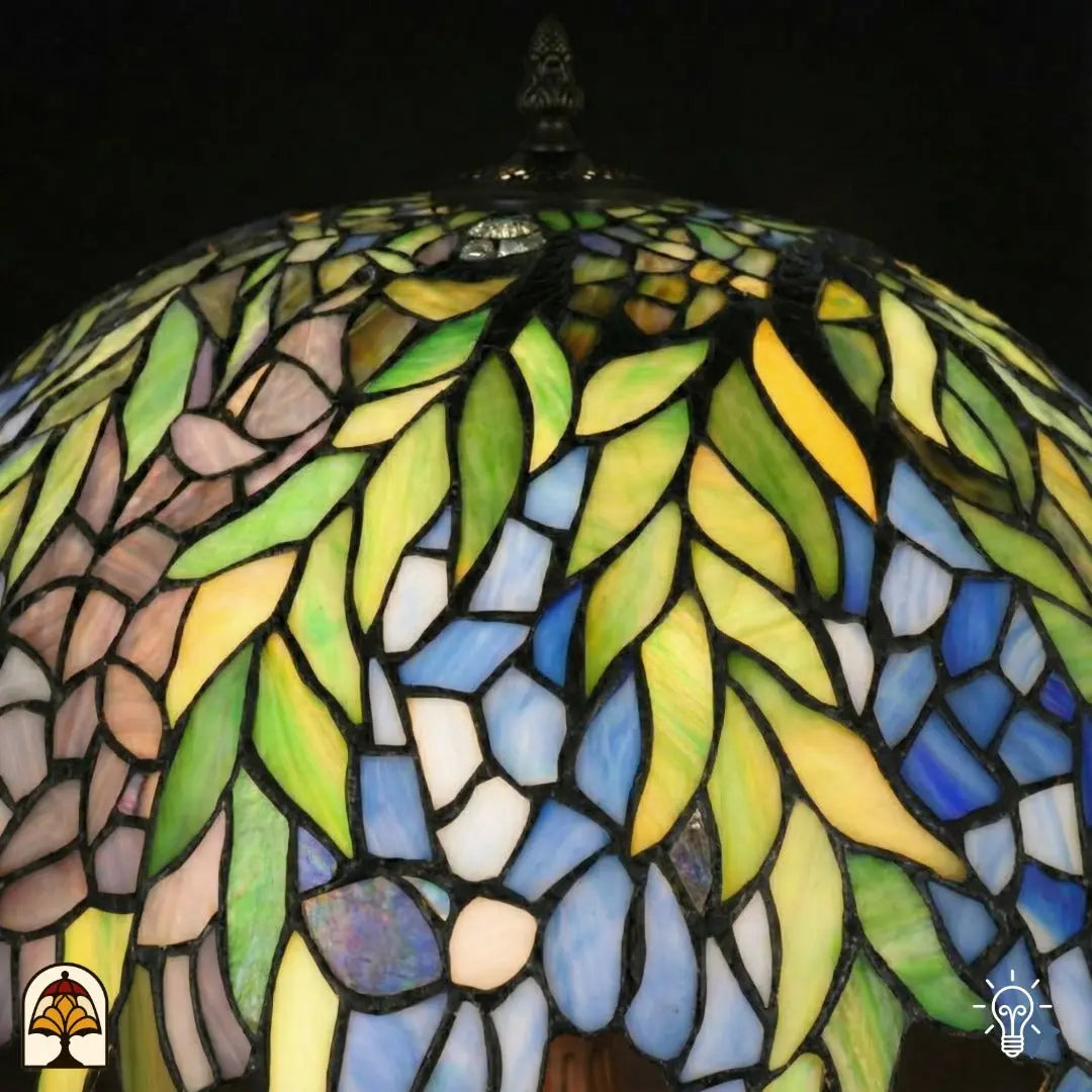 Gros plan du haut d'un abat-jour Tiffany allumé — feuilles vertes, surfaces de verre bleu/violet et jaune