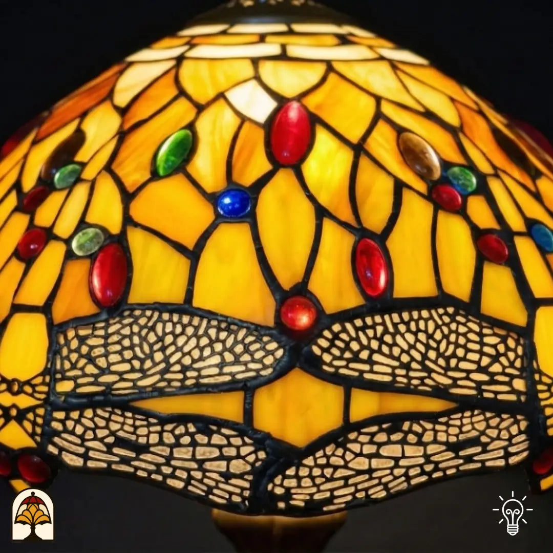Gros plan abat-jour Libellula Aurea ⌀30 allumé, panneaux de vitrail jaune doré avec cabochons ovales rouges et verts et frise de libellules le long du bord