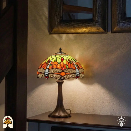 Verlichte Tiffany tafellamp Libellula Azul ⌀30 op consoletafel tegen gestructureerde witte wand, warm oranje licht op wand, spiegel met houten lijst op achtergrond
