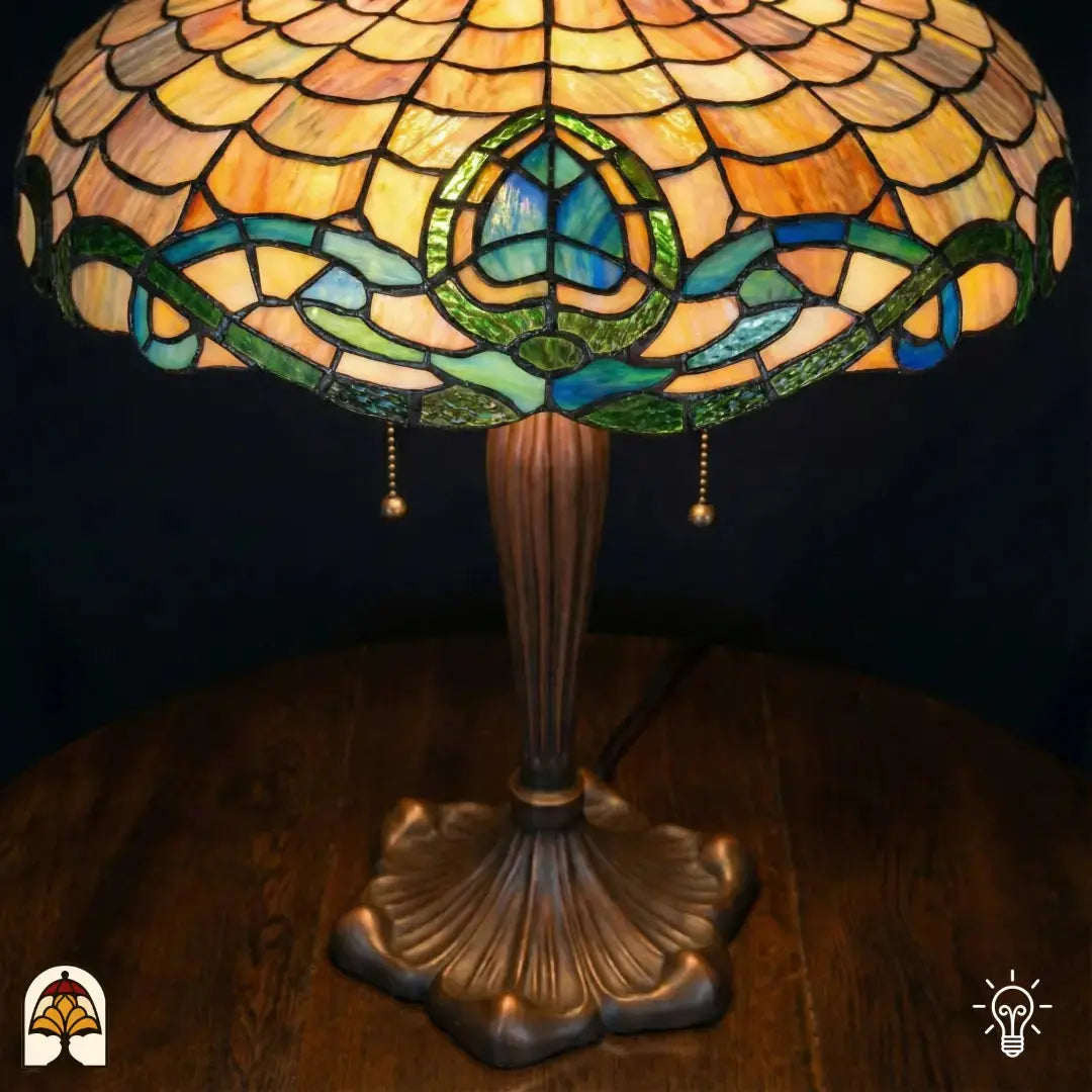 Gros plan du dessous de l'abat-jour Tiffany allumé — motif d'écailles ambré, bordure Art nouveau turquoise/bleue et verte avec motif de lotus et rinceaux de feuilles