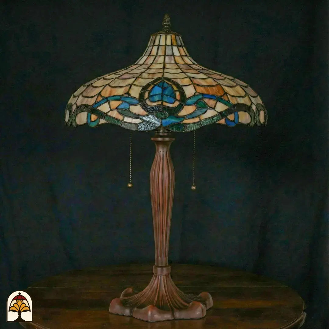 Lampe de table Tiffany éteinte sur fond bleu foncé — large abat-jour en forme de coupe avec motif d'écailles ambré, bord turquoise/bleu à motif de lotus, pied en bronze avec interrupteurs à chaînette