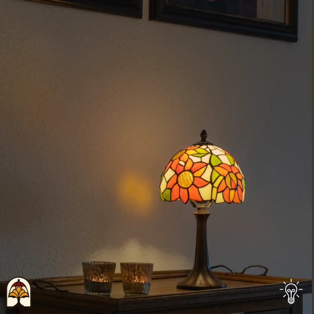 Lampe de table Tiffany Solea allumée sur un plateau en bois — lumière chaude sur un mur blanc, deux bougies chauffe-plat en verre à gauche de la lampe, tableaux au-dessus