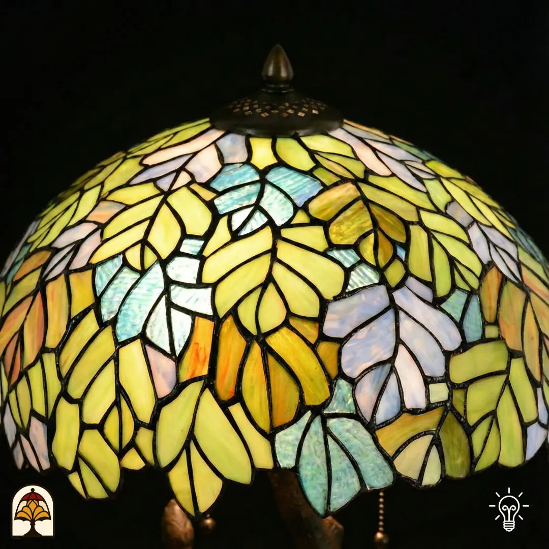 Gros plan abat-jour en dôme allumé lampe de table Tiffany Sylva Verde, motifs de feuilles jaune-vert, jaune-orange et bleu clair en vitrail