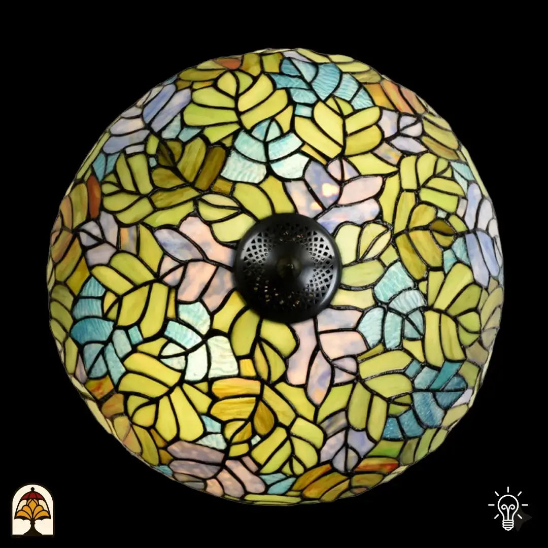 Vue de dessus abat-jour dôme allumé lampe de table Tiffany Sylva Verde, motifs de feuilles jaune-vert, bleu clair, roses et orange en vitrail, douille centrale en bronze visible